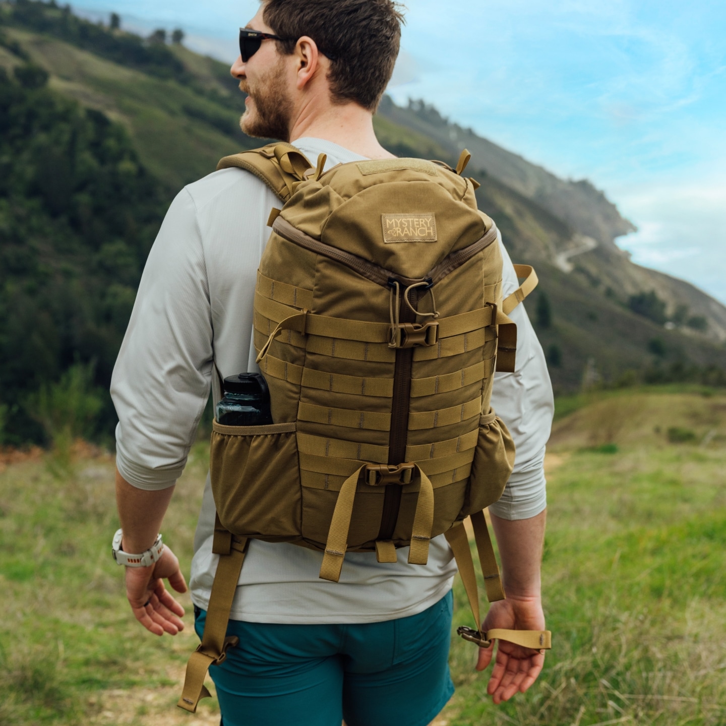 A man walking in nature wearing a Mystery Ranch backpack.